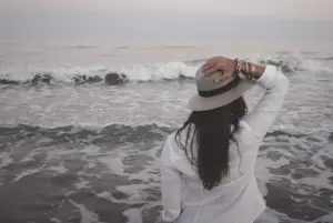 Picture of a woman holding her hat on her head in front of the ocean