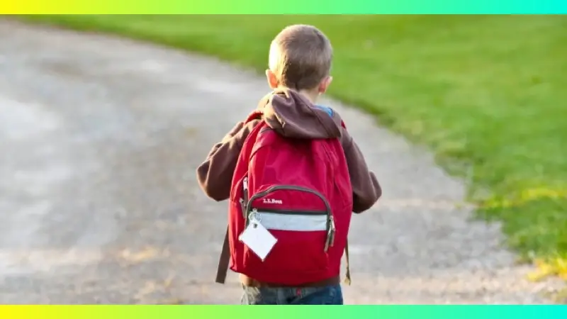 A young boy walking away wearing a red backpack