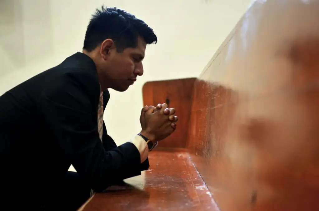 Man kneeling and praying in front of a church pew representing Dare 2 Share's blog on 4 Ways to pray for a successful, evangelistic youth group